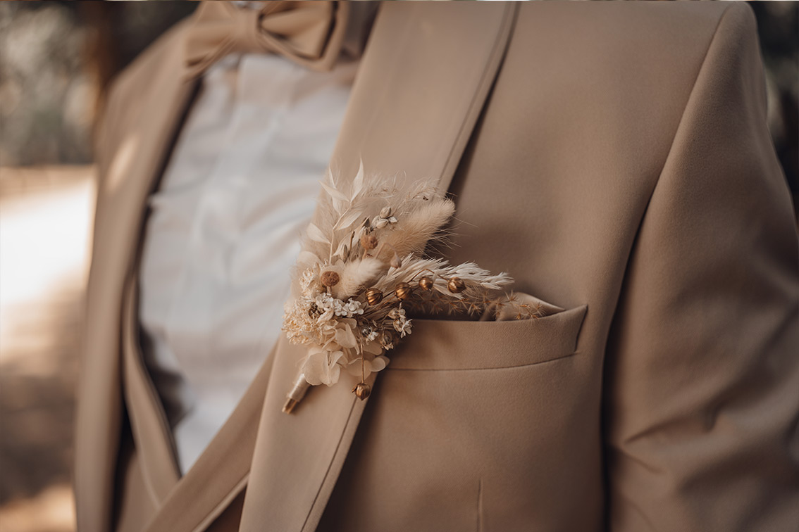 Detailaufnahme des floralen Ansteckers am beigen Hochzeitsanzug