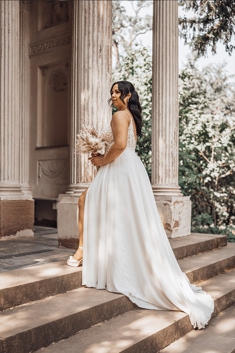 Braut steht in ihrem weißen Hochzeitskleid vor historischen Säulen